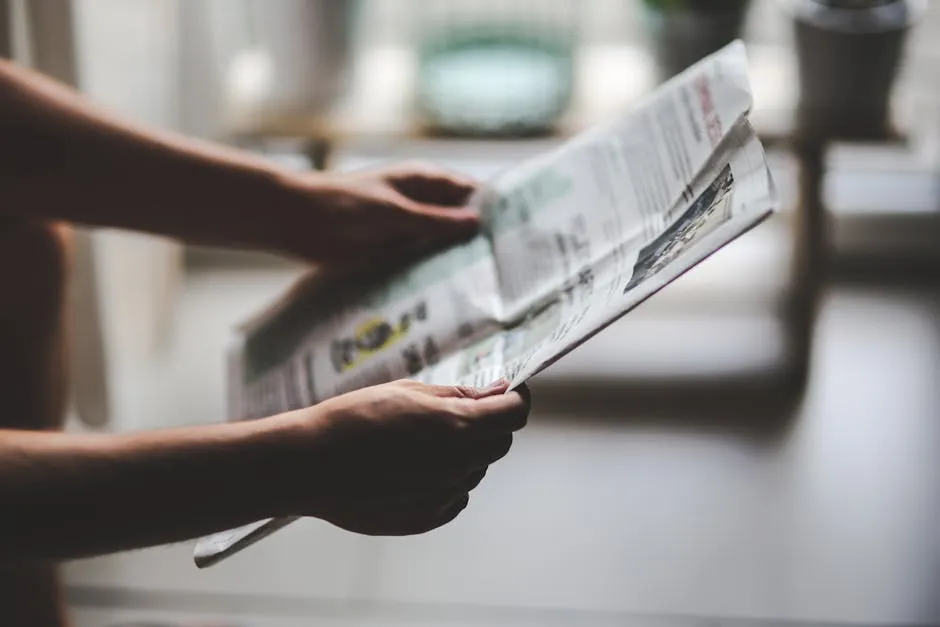 Manos sosteniendo un periódico en un ambiente cálido de lectura.